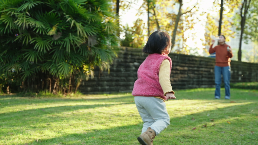 Slow motion happy asian baby girl playing together with mother in the sunny autumn yard lovely child running chasing soap bubbles on the lawn family lifestyles active kid