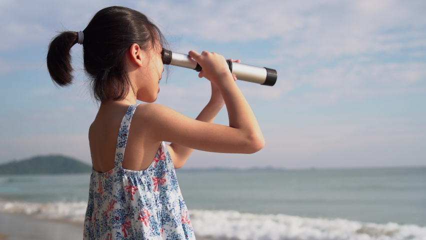 Asian child girl looking in spyglass, Happy kid playing outdoors on the beach