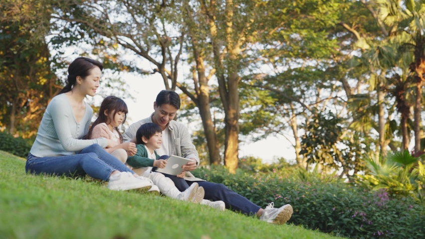 young asian family with two children sitting on grass relaxing outdoors in city park Royalty-Free Stock Footage #1082326456