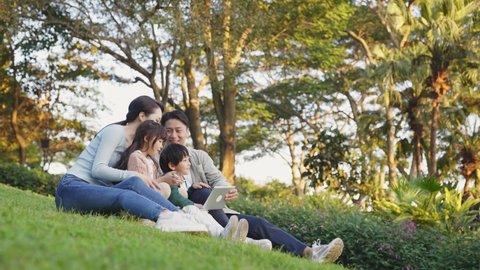 young asian family with two children sitting on grass relaxing outdoors in city park
