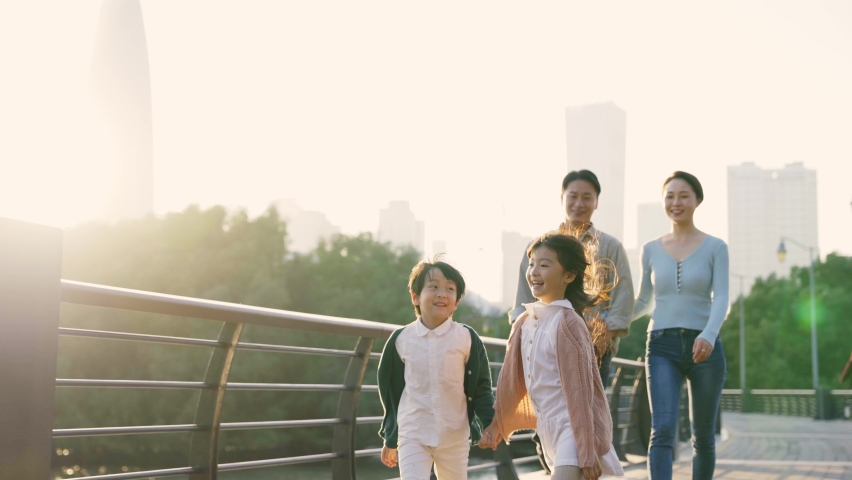 Happy asian family with two children walking on a bridge outdoors in city park