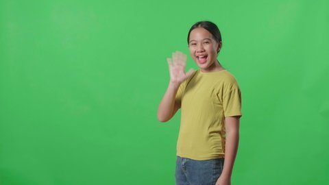 The Happy Young Asian Kid Girl Walking And Waving Hand Say Bye Bye While Standing On Green Screen In The Studio
