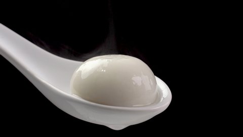 Fresh and hot Tangyuan rice dumpling ball in a white spoon over black background. Food for Winter solstice,close up shot.
