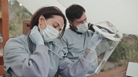Medium close-up shot of tired medical workers taking off face shields after working all day at refugee camp