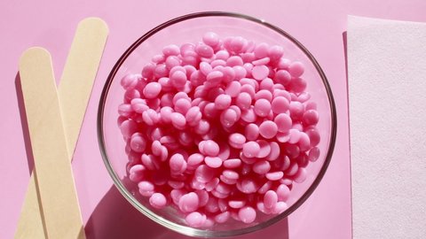 Beautiful pink depilatory wax granules, strip for depilation and wooden spatulas on a pink background. Epilation, depilation, unwanted hair removal. Top view.	