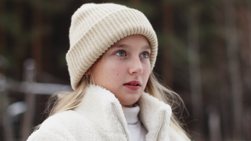 Portrait beautiful teenager white girl zip up fur jacket on winter street. Young woman in knitted hat zipping up winter jacket outdoor.