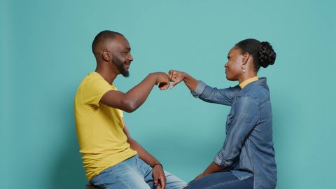 Couple sitting in studio and bumping fists together to show support and respect. Man and woman doing fist bump after deal and achievement, smiling at camera over isolated background.