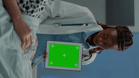 Vertical video: Analysis doctor showing tablet with green screen to patient in hospital ward at medical recovery facility. African american specialist explaining old man about canner device