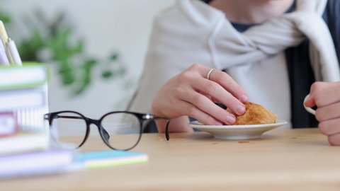 Teenage boy home online schooling. Teen schoolboy takes piece of croissant taking break during spbi video lesson via modern laptop at table in room closeup 4k video