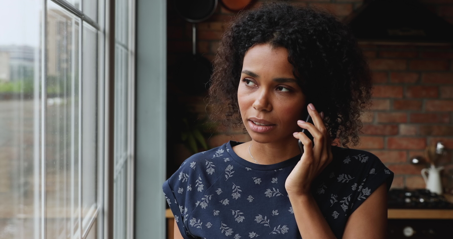 Head shot portrait beautiful 30s African woman standing in kitchen at home talking on smartphone looking out window enjoy pleasant conversation with friend use mobile connection, communication concept Royalty-Free Stock Footage #1082335627