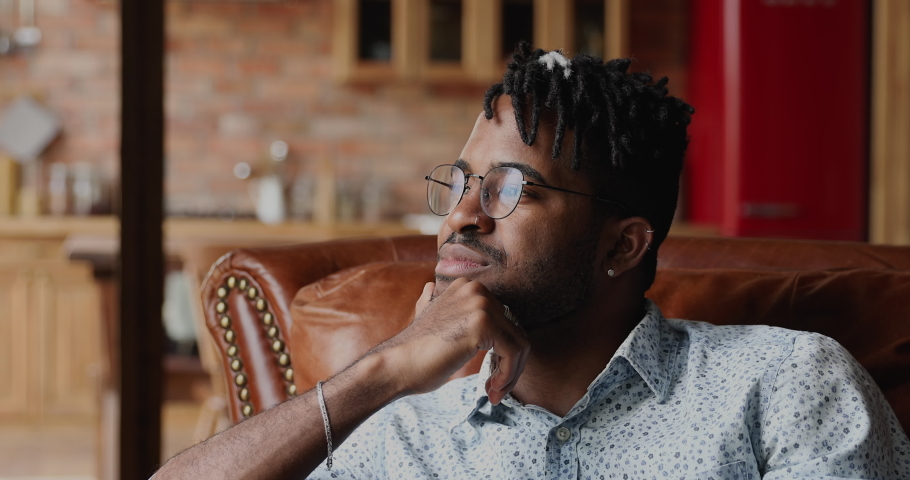 Close up profile face view portrait young African handsome hipster guy with glasses and dreadlocks hairstyle contemplate looking into distance sit alone on sofa at home. Daydreams and thoughts concept Royalty-Free Stock Footage #1082335639