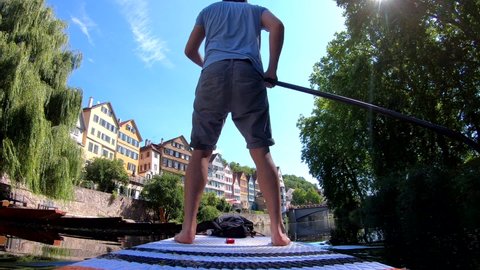 Rear-view of a man riding his stand up paddle board (SUP) down the Neckar river along the picturesque old town of Tübingen (Germany)