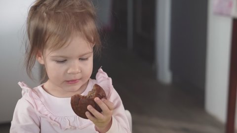 Cute little girl eats muffin at the home, close-up, slow motion. Little girl eating a cupcake with appetite.