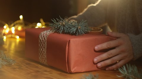 Close-up of female hands decorates Christmas gift with Christmas tree twig. Gift wrapping concept.