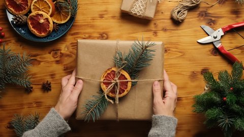 Female hands puts Christmas gift box on wooden table. Zero waste Christmas presents, gift wrapping concept. Table top view.