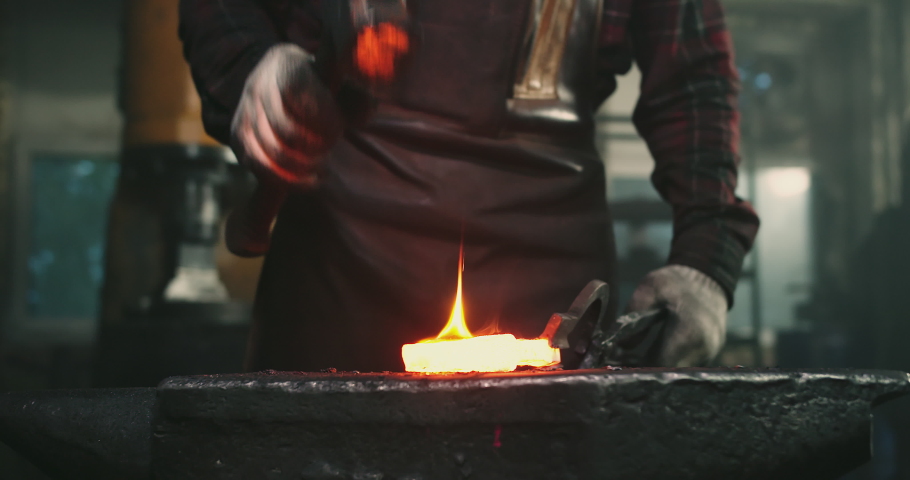 Close-up of blows on hot metal, sparks flying in different directions. The blacksmith holds the workpiece with one hand with tongs, and with the other a hammer with which he forges the product