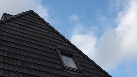 Time-lapse shot of clouds reflected in windows of residential house roof with black tiles.