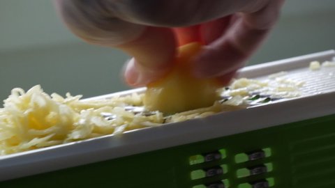 Male hands rubbing potatoes on a kitchen grater for vegetarian food cooking