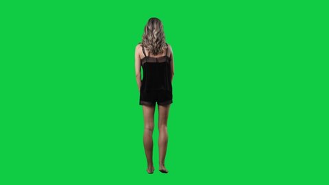 Super slow motion of young attractive woman in black satin sleepwear turning at camera tossing hair. Full body isolated on green screen background