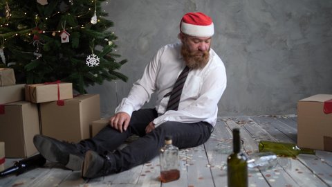 A drunken bearded man wakes up in the morning near a  tree puts on a santa claus hat and opens a box with a gift bright light comes from the box.