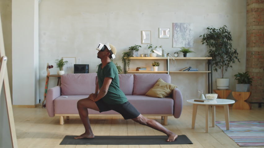 Young African American man in VR headset and sportswear practicing warrior pose on mat at home while watching yoga workout in augmented reality - Powered by Shutterstock - Get 15% off with code: PIKWIZARD15