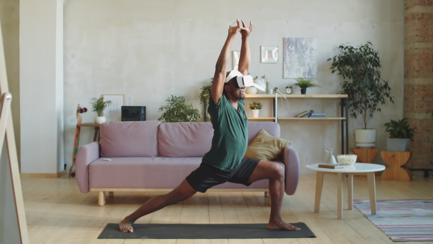 Athletic African American man in VR headset and sportswear practicing yoga on mat at home while watching online workout in virtual reality - Powered by Shutterstock - Get 15% off with code: PIKWIZARD15