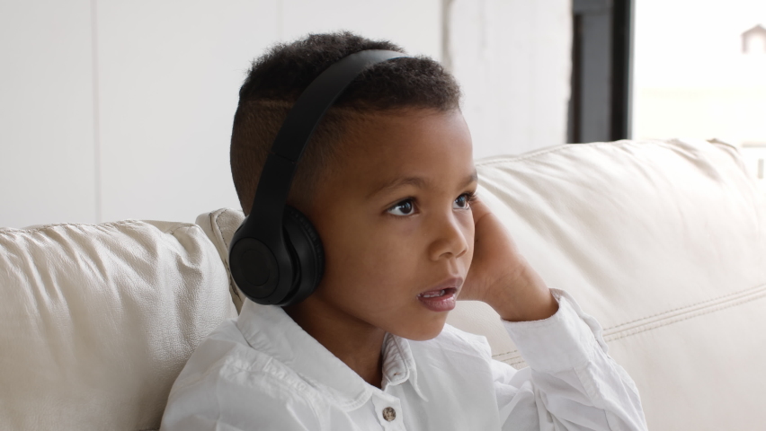Little Black Boy Wearing Wireless Headphones Listening Music While Sitting On Couch At Home, Cute Preteen African American Male Child Shaking Head While Enjoying Favorite Song, Closeup Shot Royalty-Free Stock Footage #1082351893