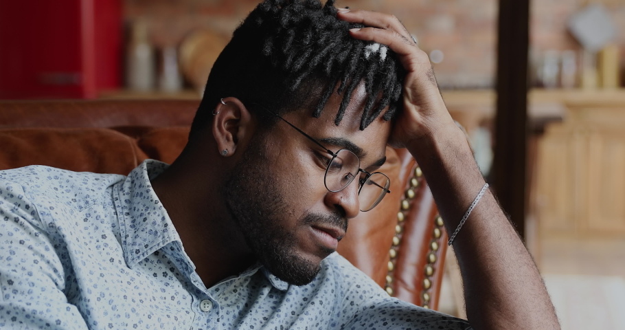 Close up African guy sit indoor look into distance deep in sad thoughts, regret the act, experiences crisis in personal life, beloved girlfriend left him, suffers from mental anguish, break up concept | Shutterstock HD Video #1082353438