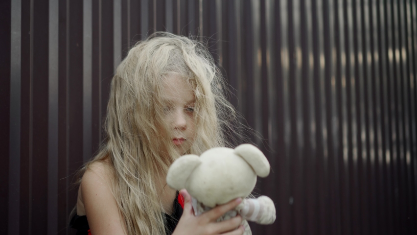 A poor, unkempt girl is playing with her doll. Her lush, tangled hair is slowly swaying in the gentle breeze.