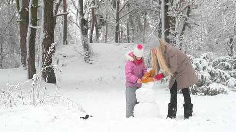 Winter fun. Happy mother with her daughter are building a snowman in a snowy park. Lovely family at winter holidays.