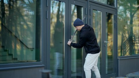 A thief burglar broke the open door of a house or office by breaking into the middle. The bandit sneaks into the building. intruder trying to force a door lock using a crowbar
