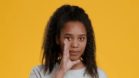 Black Teen Girl Whispering Secrets Talking Holding Hand Near Mouth And Gesturing Finger On Lips Hush Sign Looking At Camera Posing On Yellow Studio Background. Rumors And Gossips Concept
