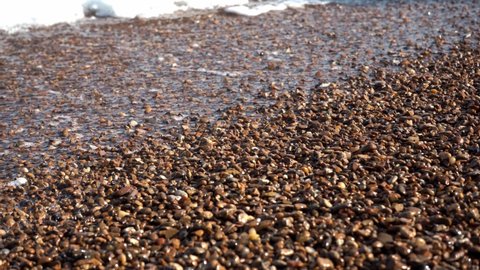 Surf sea foam and shiny smooth pebbles. The sea wave foamed and covered the pebble beach.