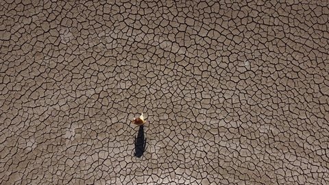 Wide aerial view of a girl walking alone across a dry, barren landscape during a drought in Cyprus, Greece.