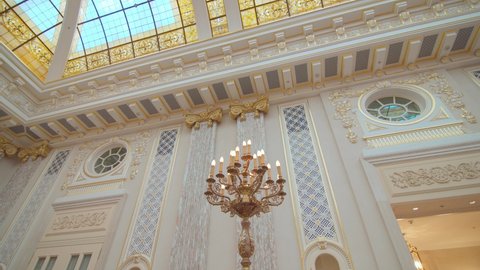 beautiful interior with light patterned walls and a high glass ceiling, large gilded candlestick with electric lamps. wide angle dolly shot, bottom top view. royal style hall
9.23.2021 Kyiv, Ukraine