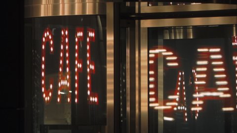 Cafe red glowing sign reflected in glass. open nightclub entrance, revolving transparent door.