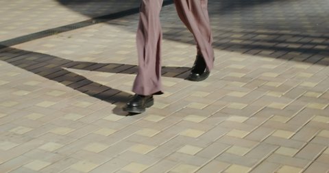 Women's legs in classic business wide-cut pants and black massive booties are walking along the sidewalk, close-up