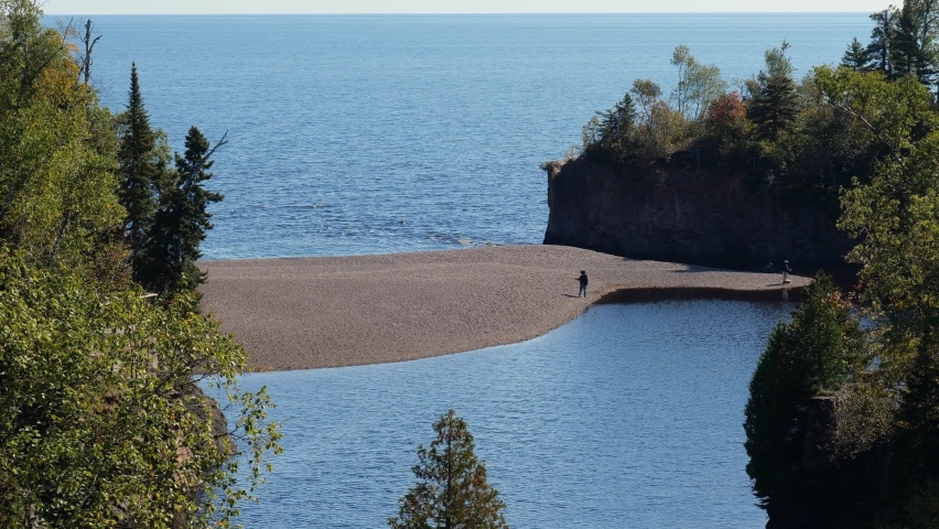 Mouth of the Baptism River where it enters Lake Superior in Minnesota, with a couple people fishing from as sandbar. At Tettegouche State Park on the shore of one of the Great Lakes.