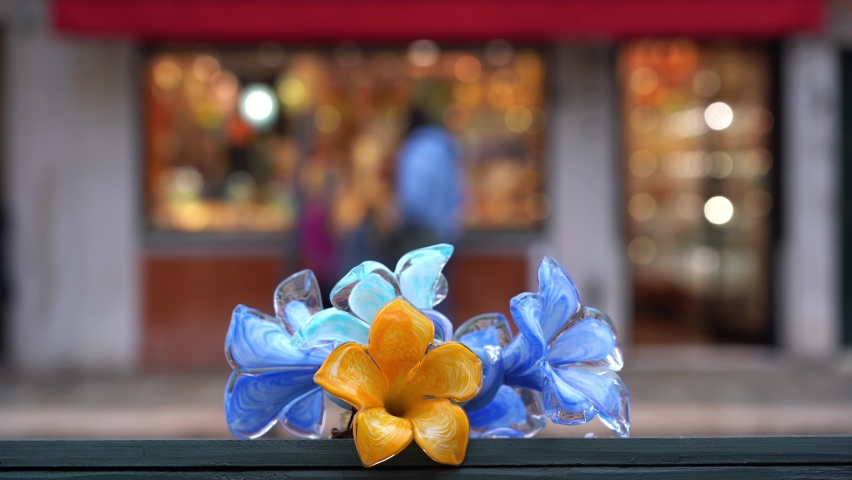 Ornamental glass artifact produced in Murano with the shape of flowers and souvenir shop behind it -  Europe, Italy, Venice 