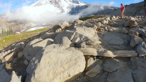 4K video tilting up from rock trail to reveal hiker looking out at the ice covered volcano peak of Mount Rainier in the Pacific Northwest