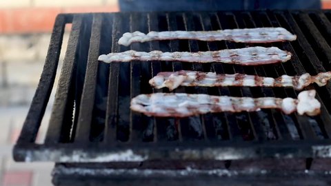 The chef flips slices of fried bacon on the grill