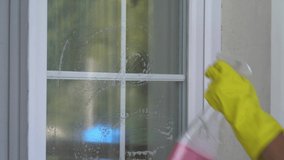 A woman's hand wipes the surface, washes the windows of a cozy home with a pink sponge and a rag, close-up. The girl is cleaning the house.