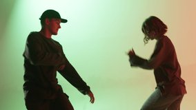 Professional choreographers dancing hip hop on color changing neon background. Man and woman dancers showing movements, pair dance, duet. Modern dance school for teenagers.