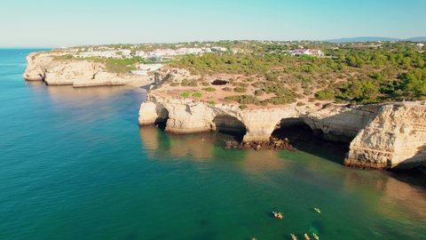 Aerial view of Benagil Caves with kayaks swimming in blue oceanic waters in 4K. Algar de Benagil, coastal view from above on a beautiful sunny day with people relaxing on holiday in a residential area