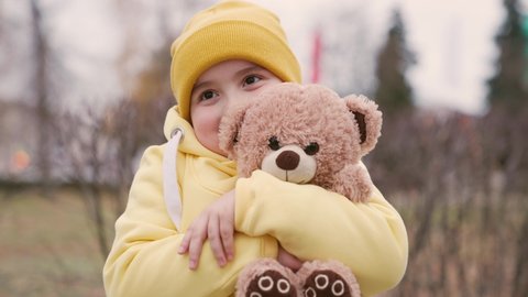 The child plays with the Teddy bear. Little girl hugs her favorite stuffed teddy bear on the playground. Plush toy in the hands of a kid in the autumn park. The kid plays with a toy. Best friends
