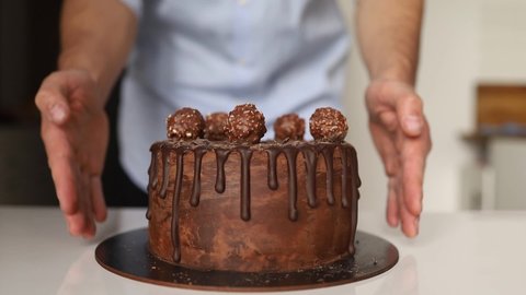 male baker putting chocolate on cake at workplace. Young confectioner finishing dessert on plate at kitchen.