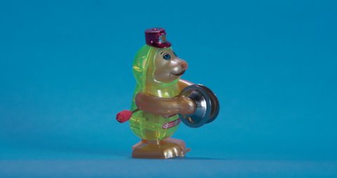 Toy wind up figure monkey with hat hits cymbal cymbals drums and goes to it in a circle in front of a blue background