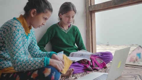 Two young village or rural school girls sitting indoors and using the laptop with the internet to study in an interior house set up with the green mountains in the back. learning and education concept