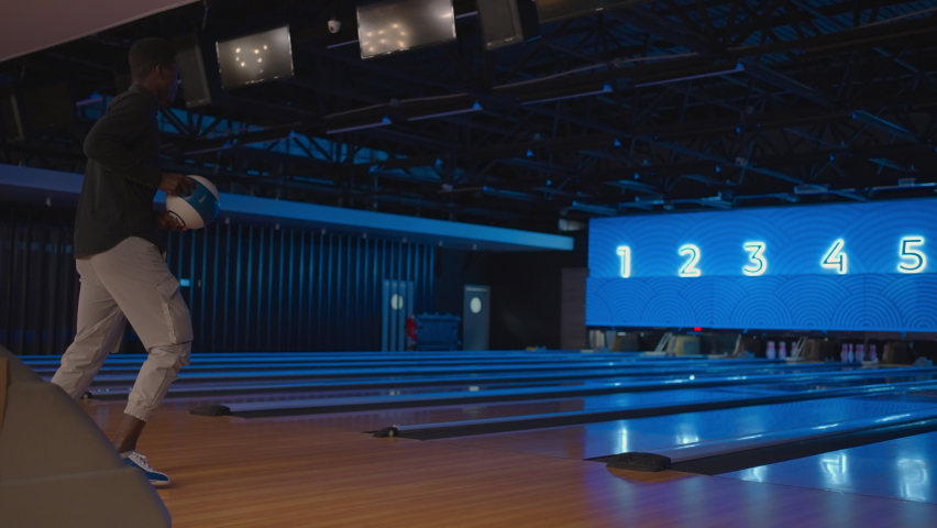 A black man bowling man throws a ball in slow motion and knocks down skittles. Play bowling. Throw balls on the floor of the bowling club