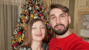 Young multiethnic couple making videocall online in front of christmas tree using smartphone. High quality 4k footage